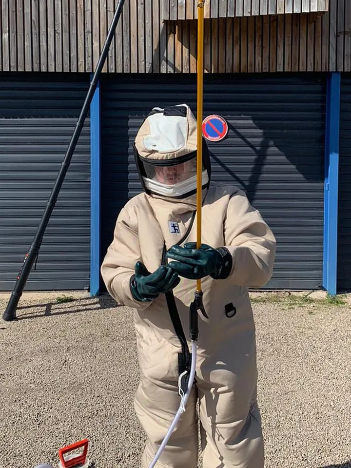 Technicien de 3D Nuisibles Alsace en combinaison int&eacute;grale de protection, avec perche t&eacute;lescopique, avant la destruction d'un nid de gu&ecirc;pes